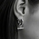 A close-up of a person's ear wearing a silver crescent hoop earring with a small toggle clasp, shown against dark brown hair.